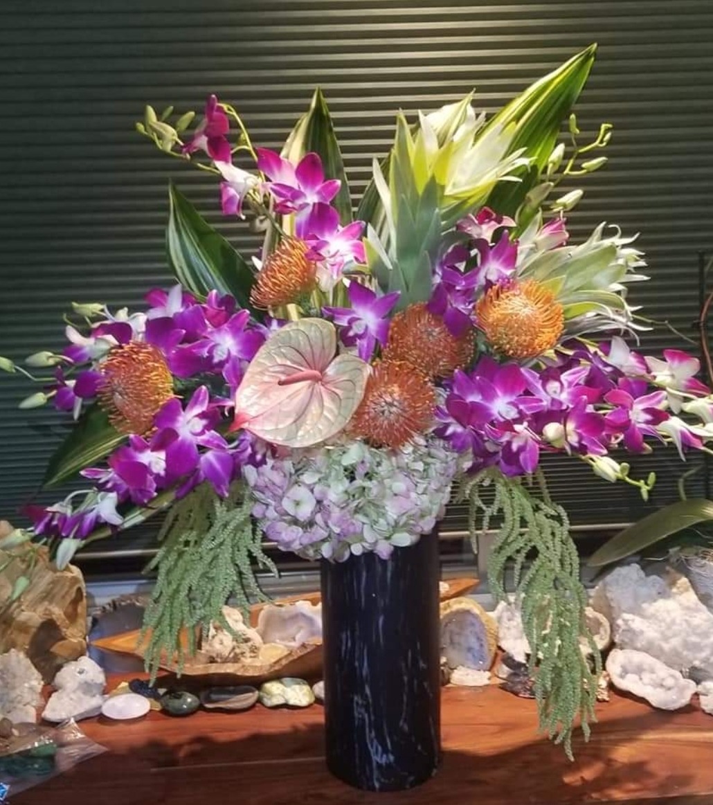 Vibrant floral arrangement featuring purple orchids, tropical foliage, and unique blooms in a sleek black vase, showcasing artistry in floral design.