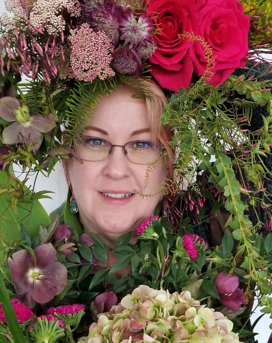 Woman surrounded by vibrant flowers, including roses and greenery, showcasing floral artistry and design. This image highlights creativity in flower arrangements.