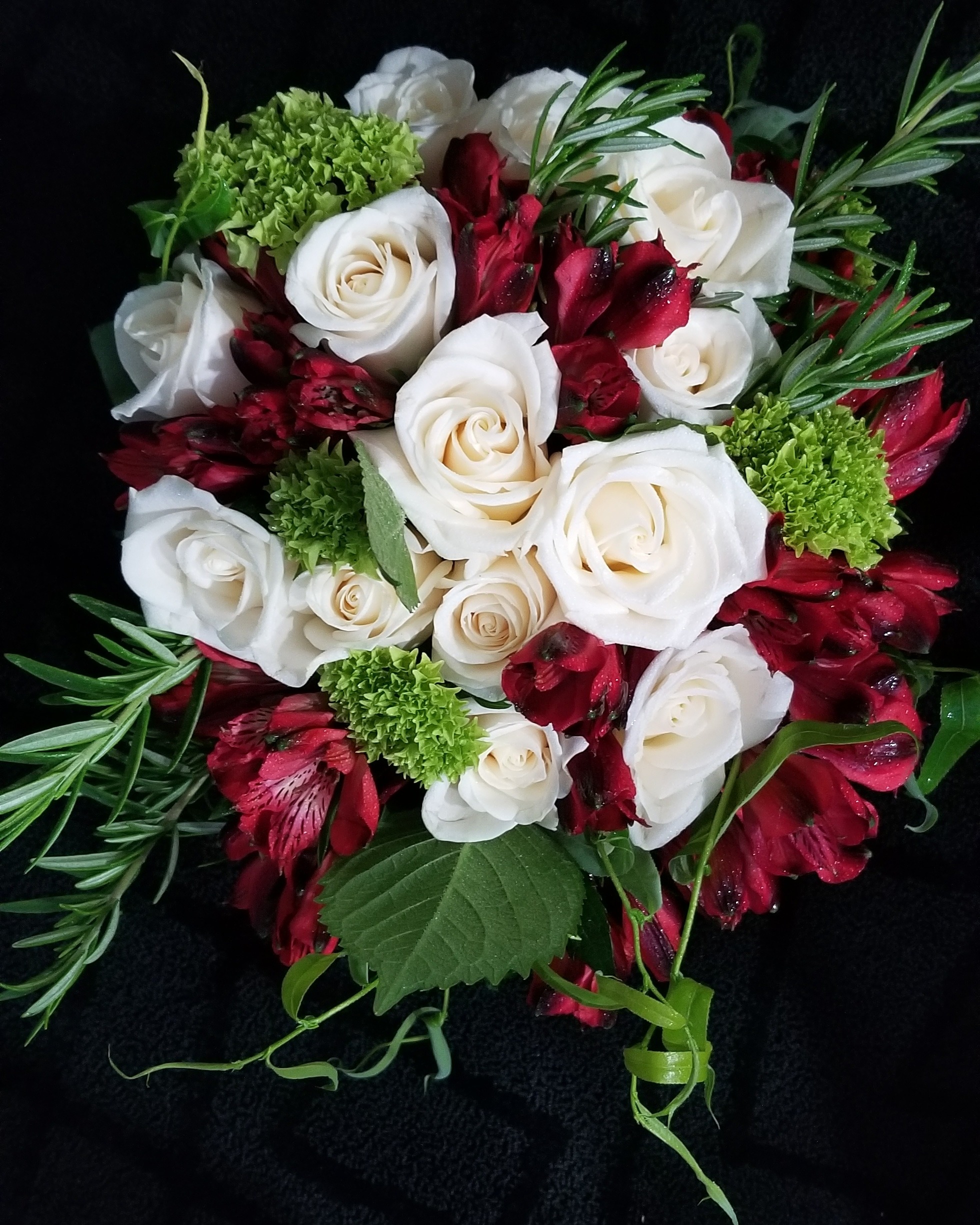 A vibrant bouquet featuring white roses, deep red alstroemeria, and green decorative accents, arranged artistically on a dark background.